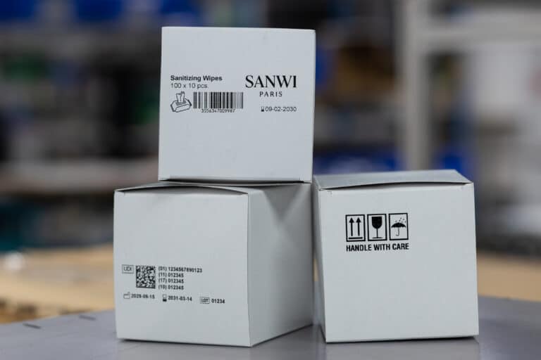 Barcode, UDI-Code, Haltbarkeitsdatum und Versandsymbole direkt auf weißen Kartonverpackungen gedruckt