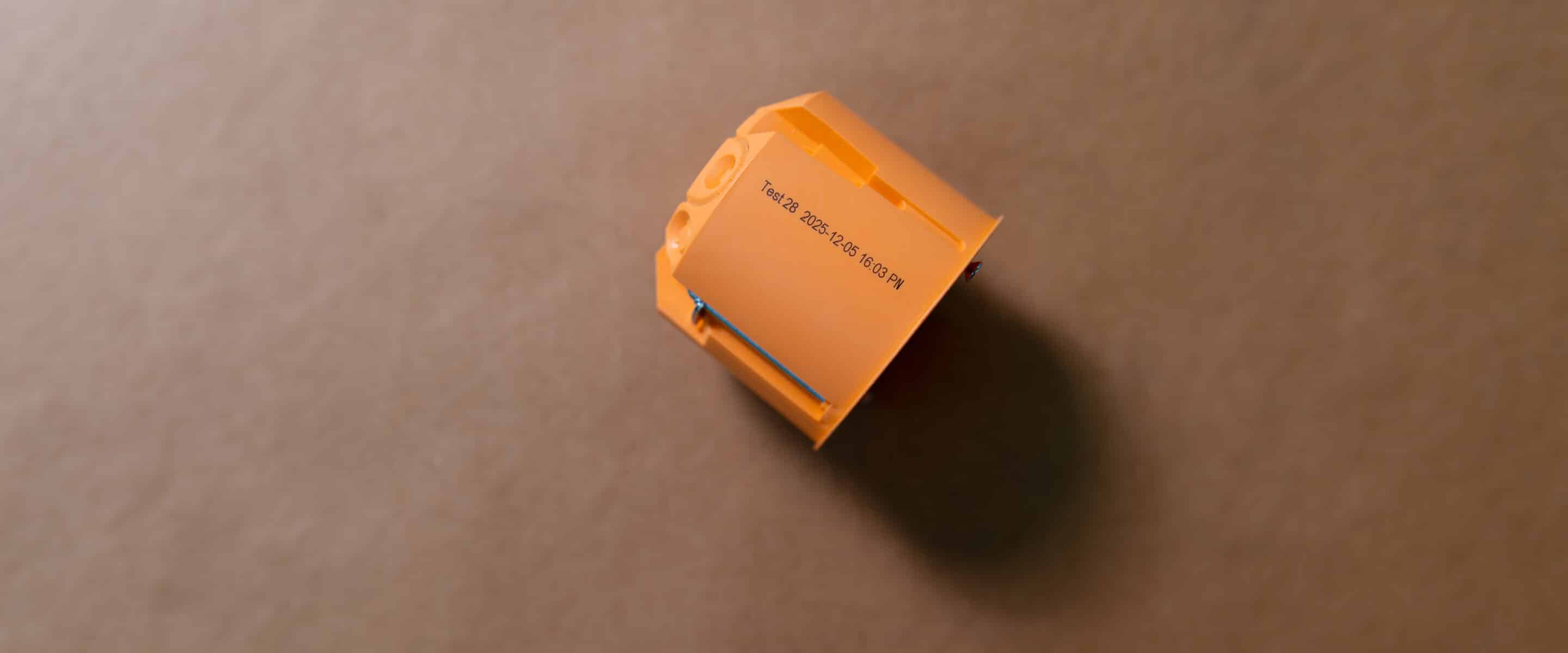 Orangefarbenes Kunststoffbauteil mit aufgedruckter Kennzeichnung