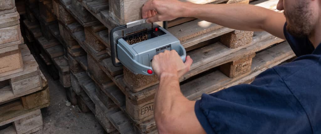 Une personne marque des palettes en bois empilées à l'aide du jetStamp 1025 mobile de REINER.