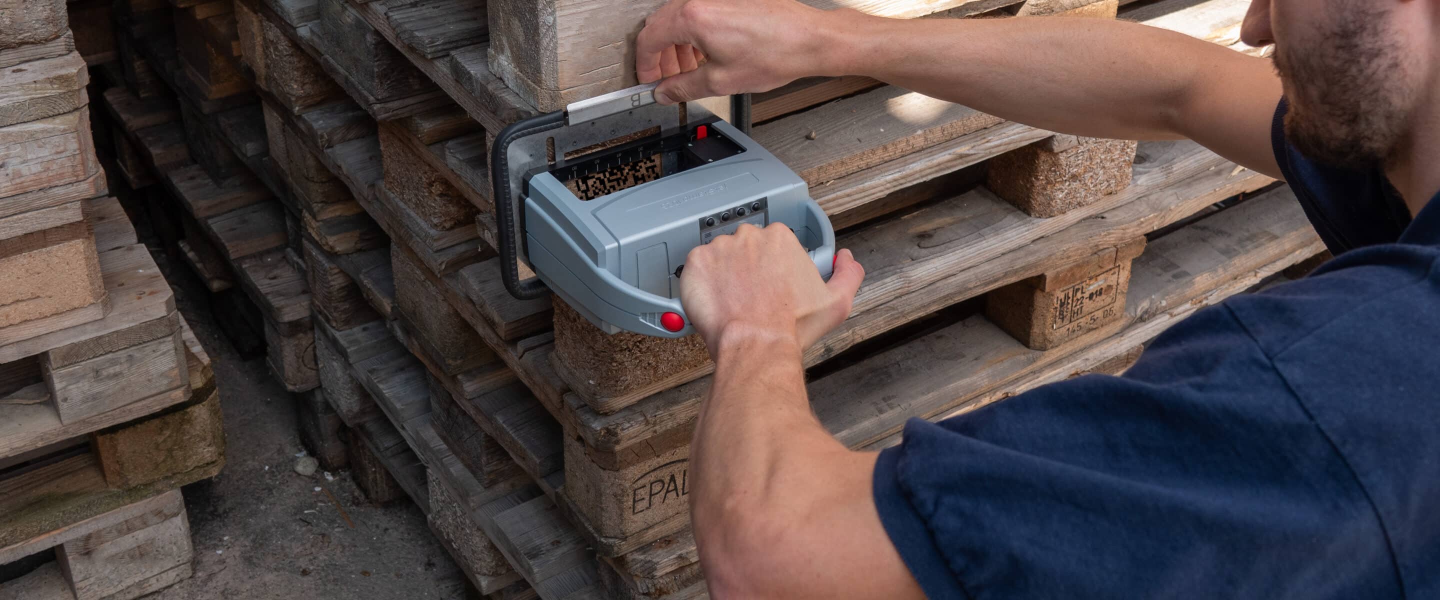 Une personne marque des palettes en bois empilées à l'aide du jetStamp 1025 mobile de REINER.